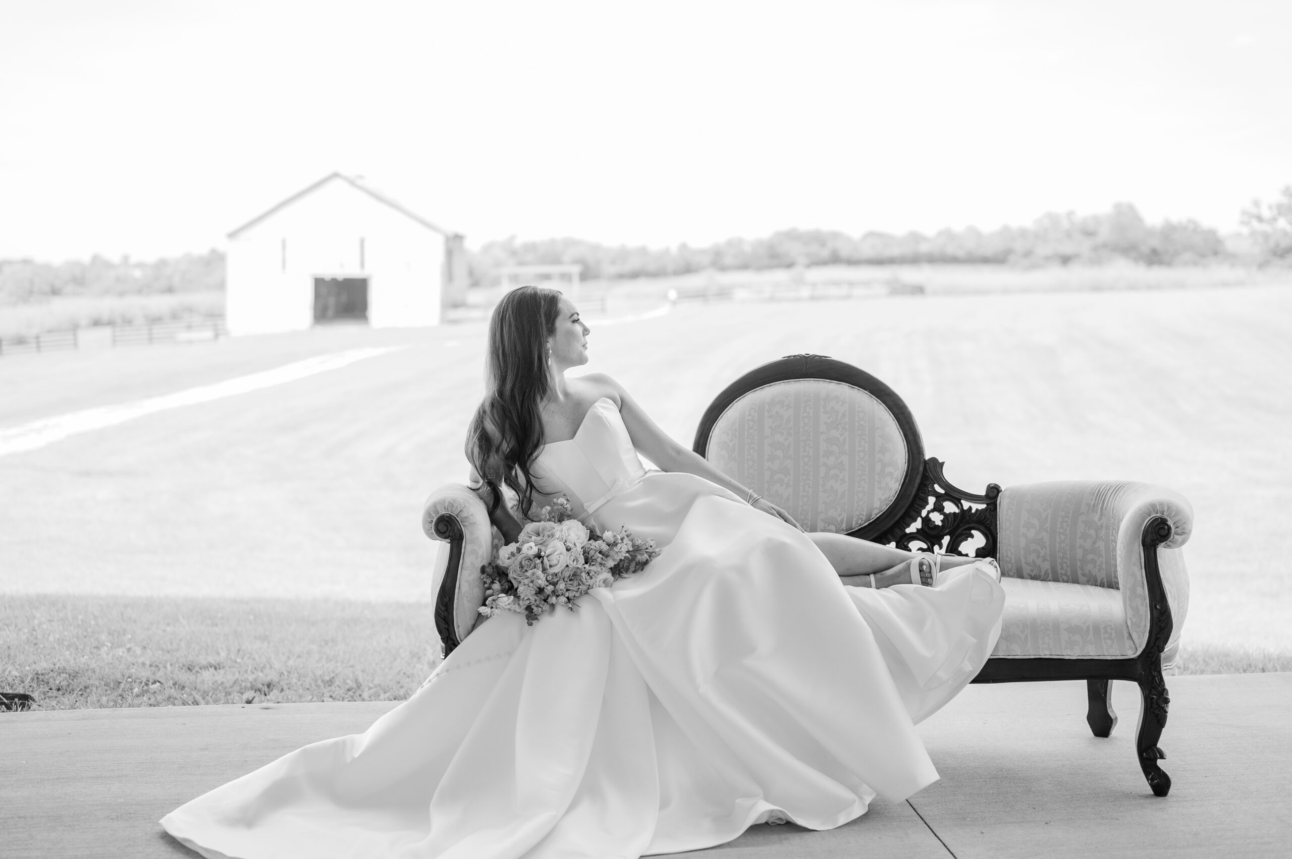 Bride Sits on Antique Couch in Ball Gown Wedding Dress looking over her left shoulder