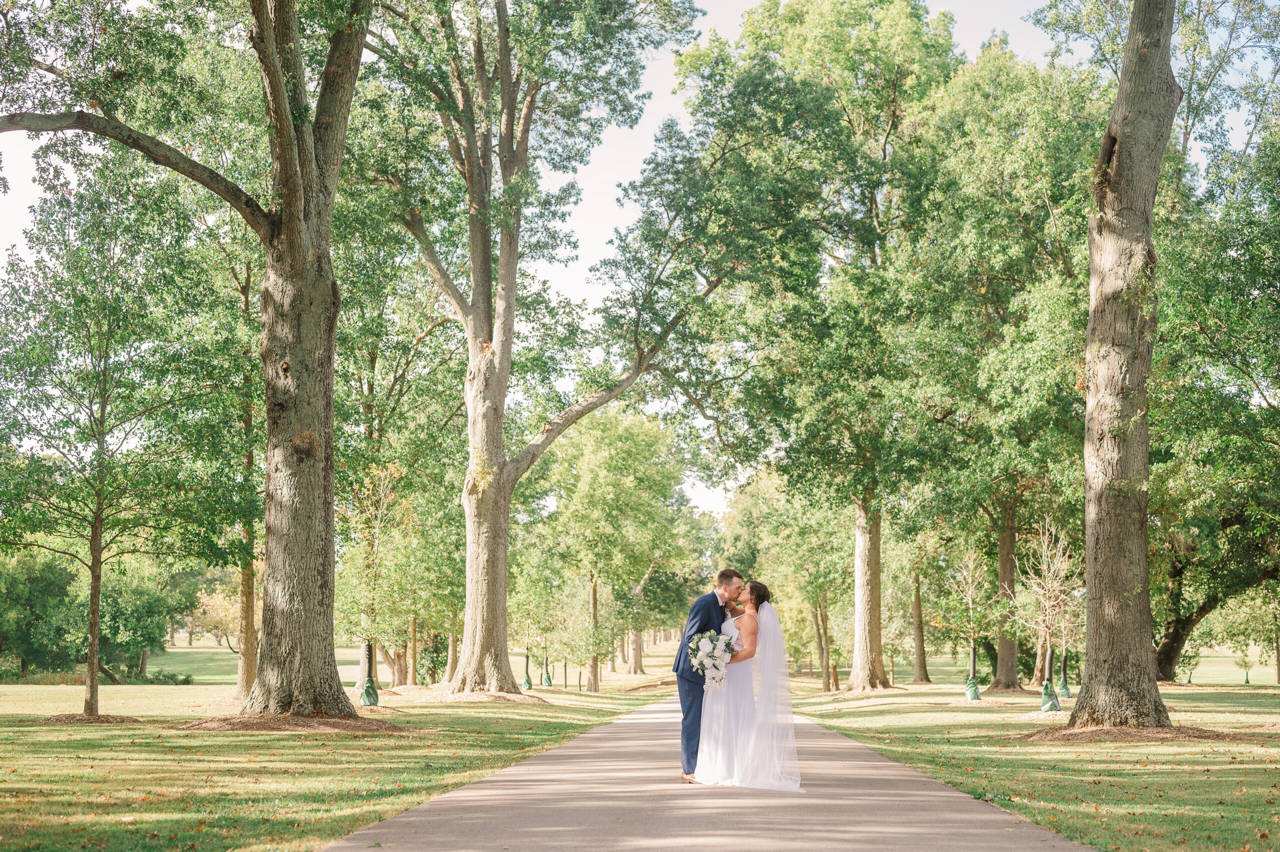 Bride and Groom walk down tree lined driveway and share a kiss while the groom dips the bride
