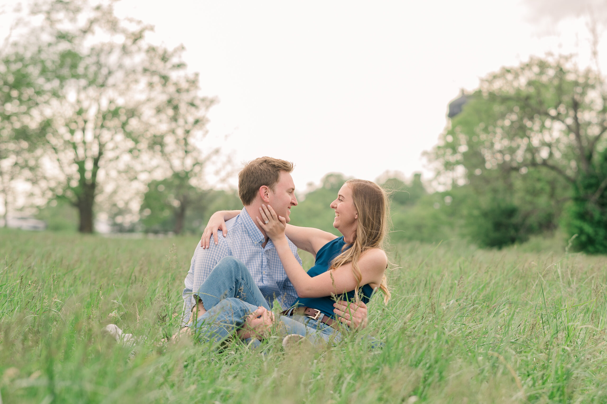 A couple sits in the grass at Keenland Race track laughing during their engagement photos